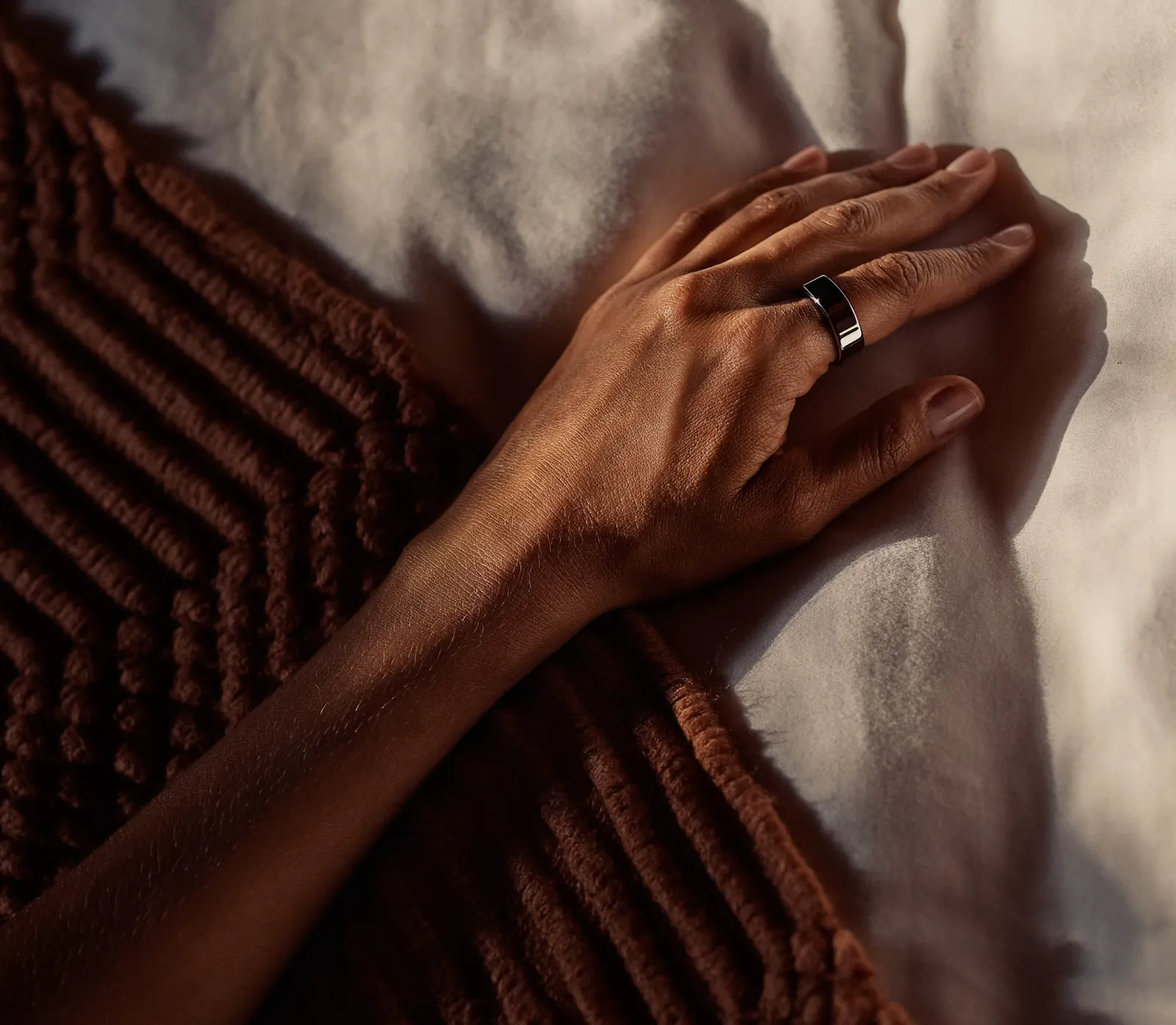 Une main sur un lit, la KEORA Ring au doigt.
