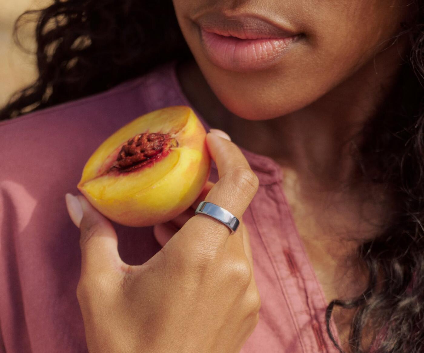 Gros plan sur une personne tenant un fruit, la KEORA Ring 6 Silver au doigt.