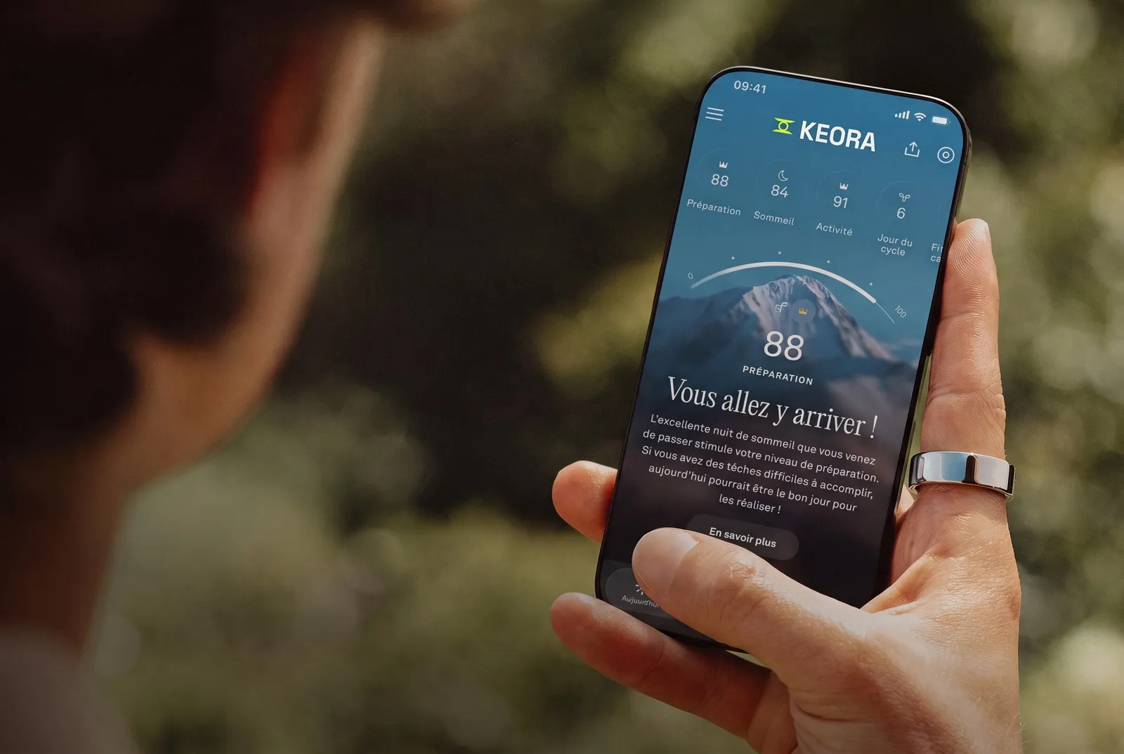 Une personne consulte l'application KEORA sur son smartphone, la KEORA Ring à l'index droit