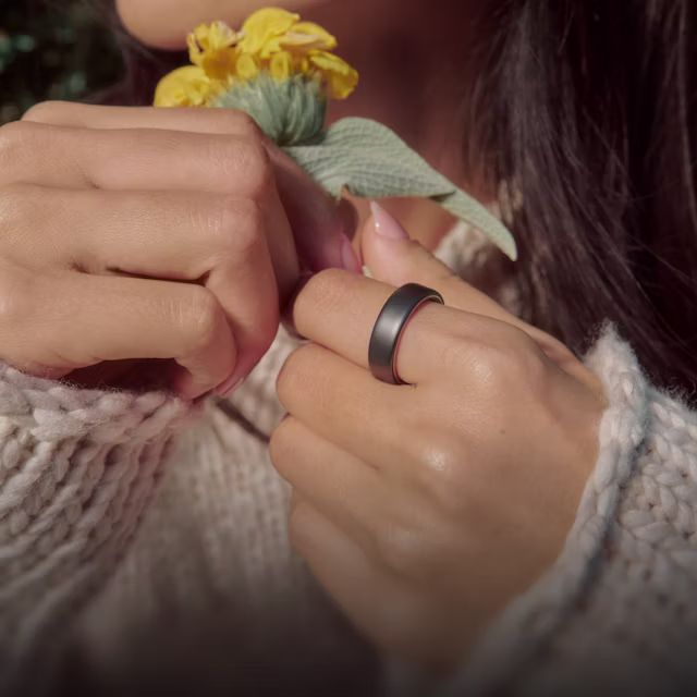 Gros plan sur la main d’une personne tenant une fleur, la KEORA Ring 6 Stealth au doigt