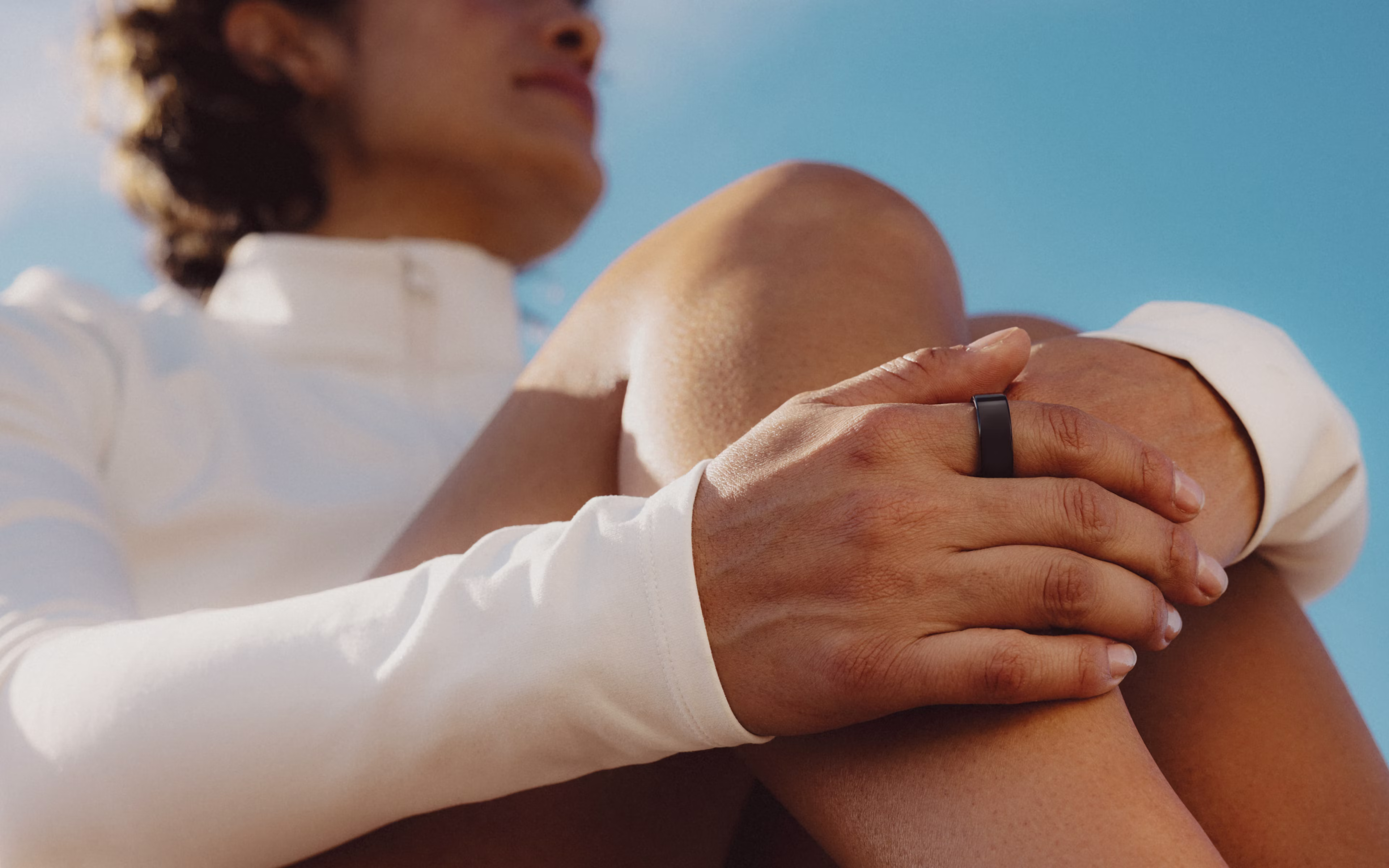 Femme assise, la main posée sur son genou, la KEORA Ring au doigt, avec superposition de l'application
